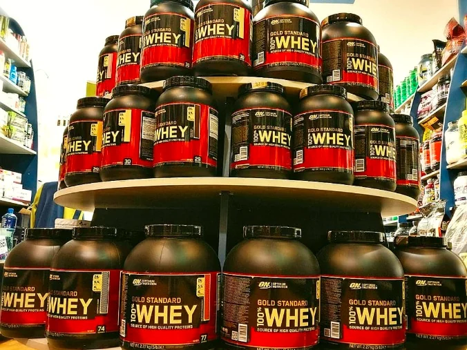 A tiered stand stacked with red and black Gold Standard whey protein tubs
